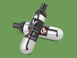 Two aerosol spray cans with a black and silver design, featuring hazard symbols, on a green background.