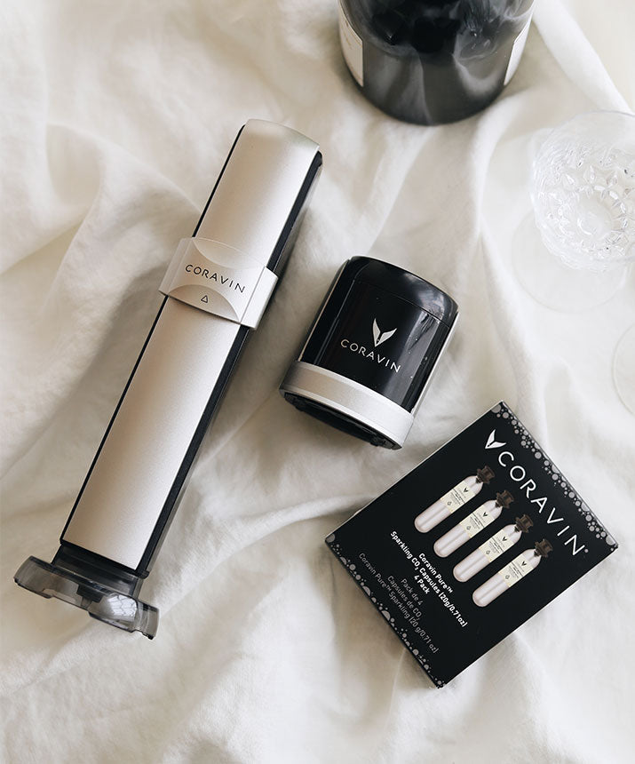 Coravin wine preservation system, black canister, and a box of three sparkling wine gas cartridges on a white cloth background.