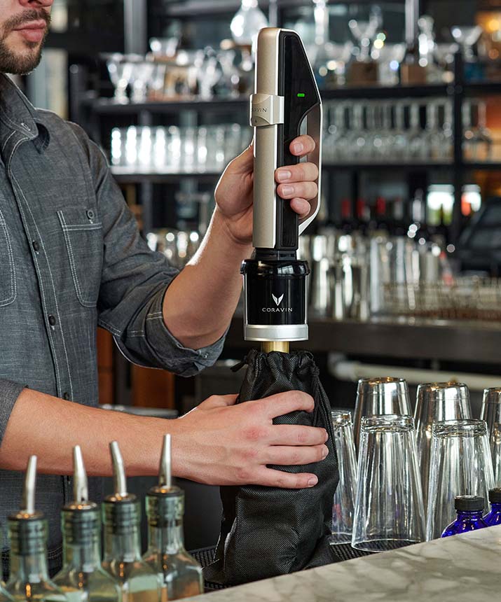 A bartender uses a Coravin wine tool to pour wine from a bottle while keeping it sealed and fresh.