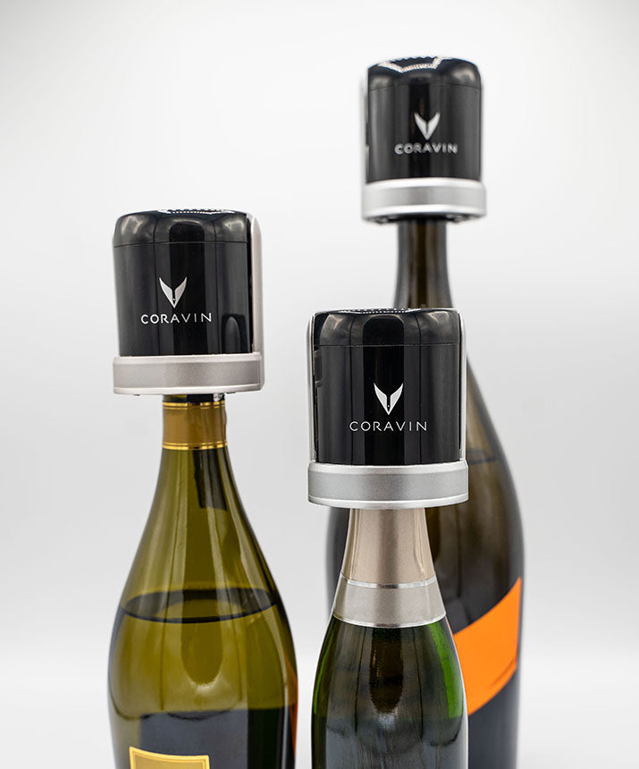 Three wine bottles with Coravin wine preservation devices on top, featuring the Coravin logo prominently displayed.
