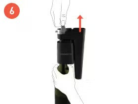 Hand positioning on a black bottle opener as it is being lifted off a wine bottle, with an arrow indicating upward motion.