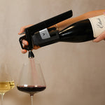 A hand holding a wine aerator pours red wine into a glass, with a white wine glass next to it.