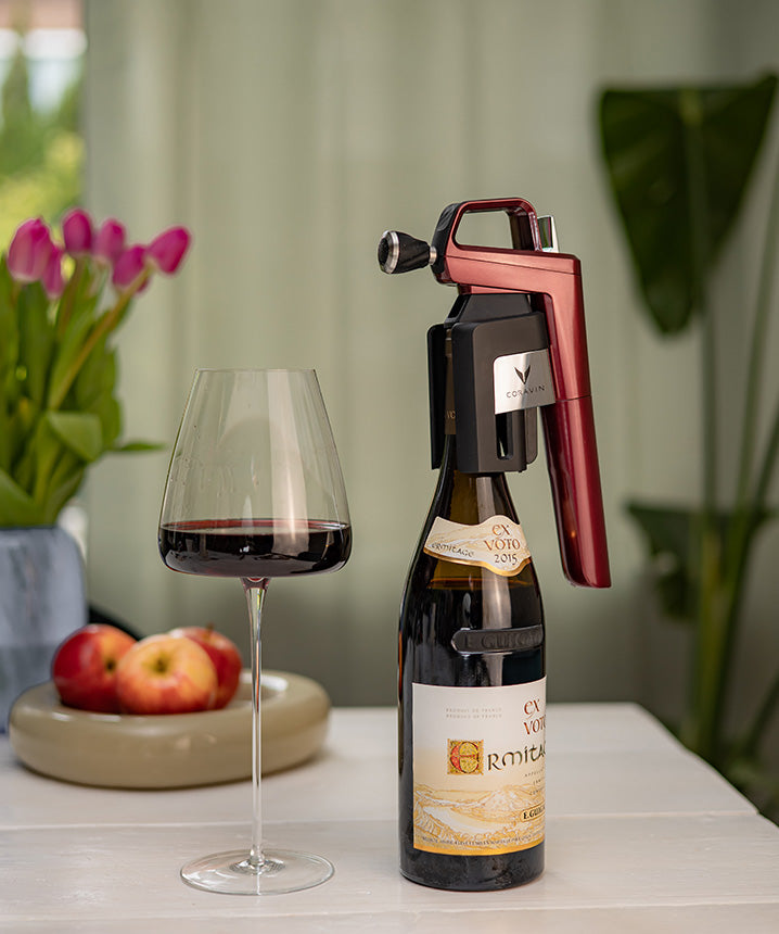 A Coravin wine opener perched on a bottle of 2015 Ex Voto Hermitage, next to a glass of red wine and fresh apples.