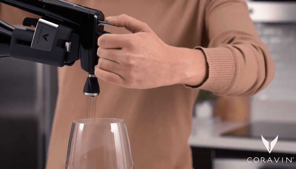 A person using a Coravin wine opener to pour wine into a glass, showcasing the pouring mechanism.