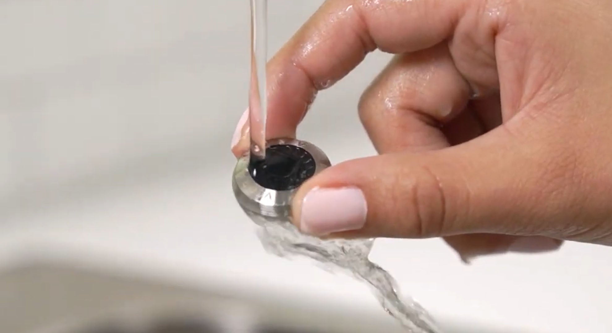Hand holding a silver faucet aerator under running water, illustrating water flow through the fixture.