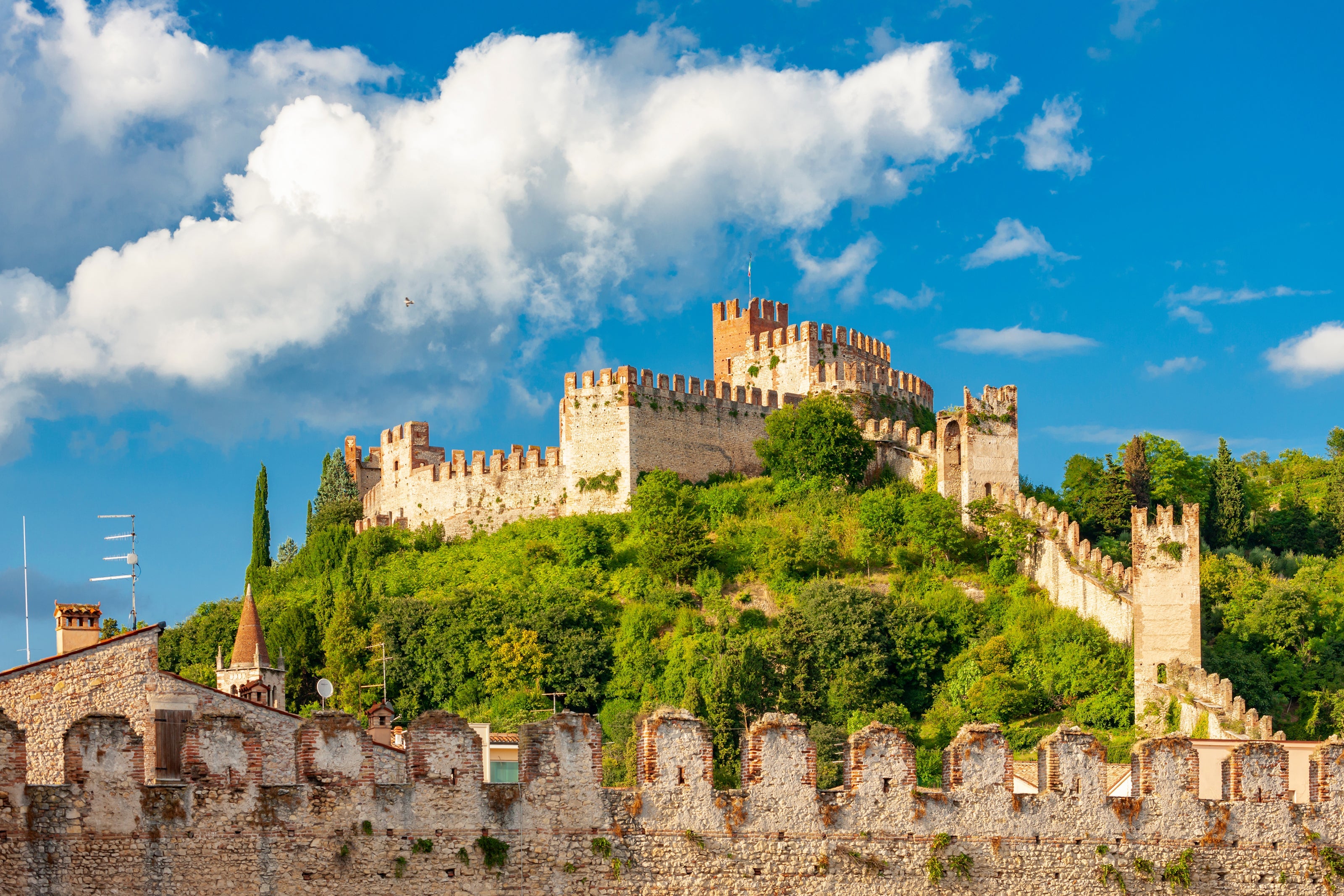 Medieval Soave Castle atop a lush green hill under a bright blue sky in the Veneto wine region of northern Italy.