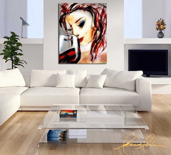 Modern living room with a white sectional sofa and glass coffee table, featuring a vibrant wine-themed painting of a woman with red hair savoring a glass of red wine by Leanne Laine.