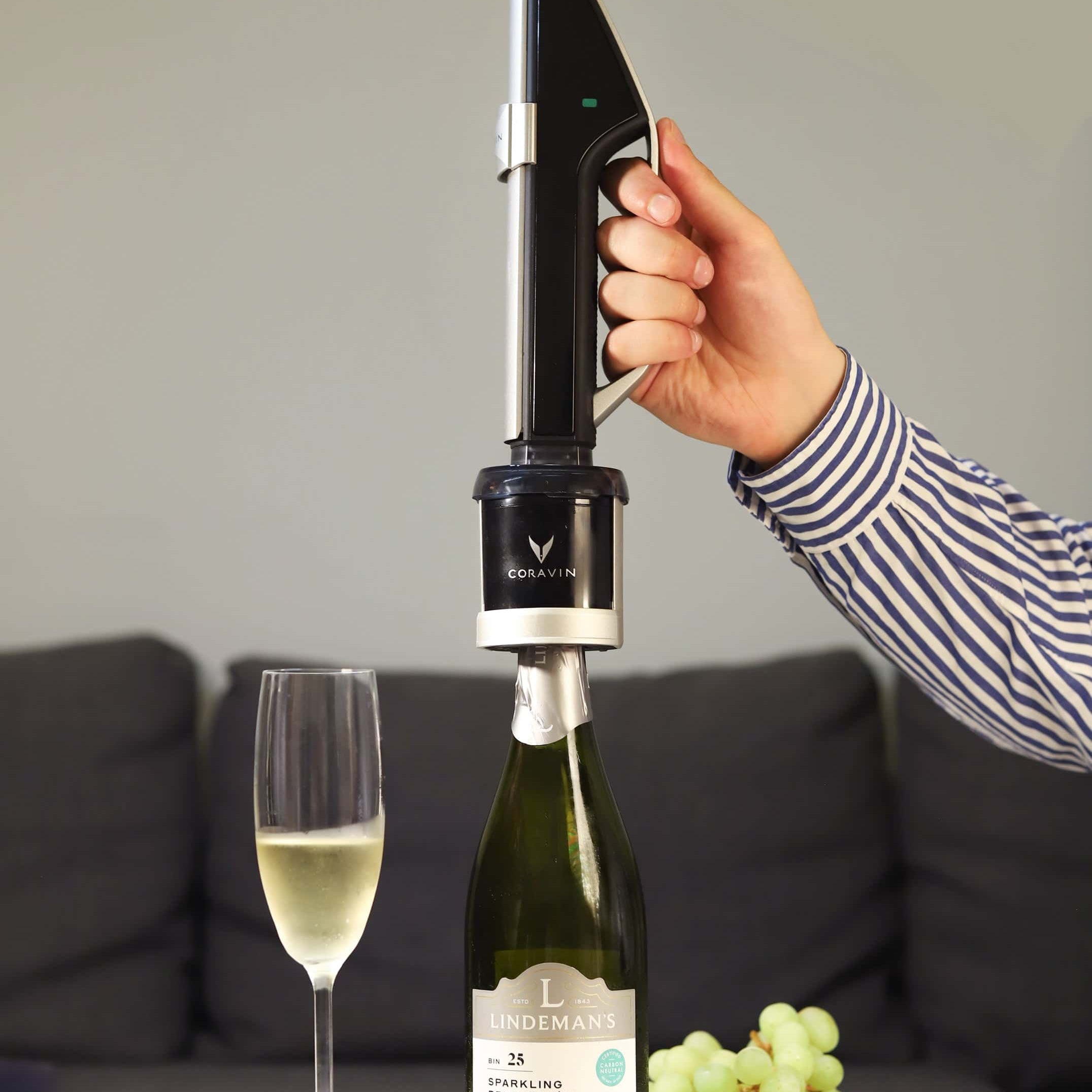 Preserving a bottle of Lindeman’s Sparkling Brut Cuvée using the Coravin Sparkling Wine Preservation System, with a glass of sparkling wine, strawberries, and grapes on a white table.