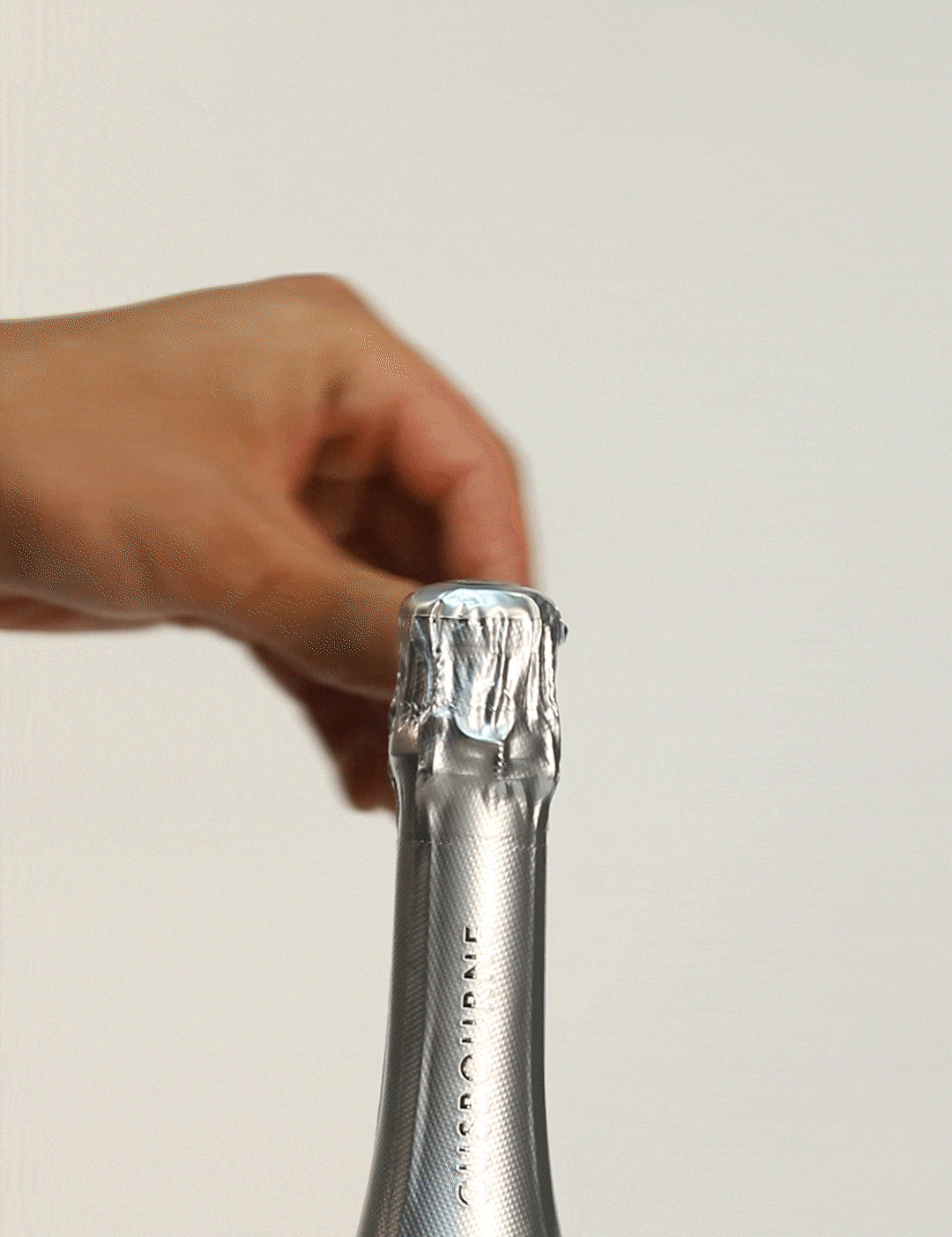 A hand removes the foil from a sparkling wine bottle, revealing a silver neck and label details.