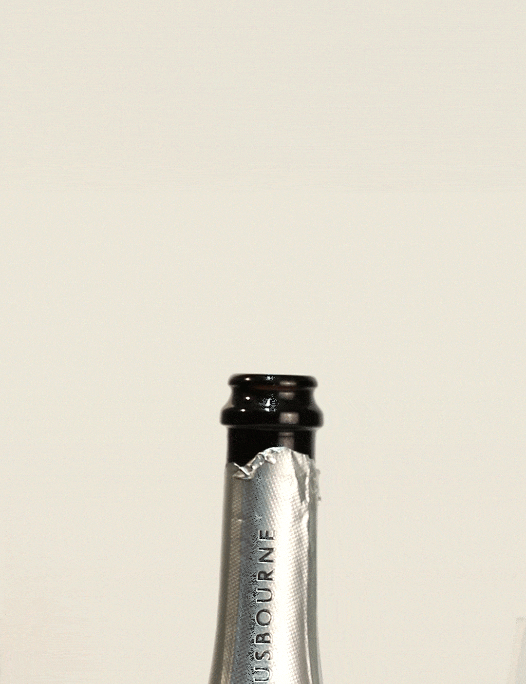 Close-up of a champagne bottle neck, featuring a silver label with "Gusbourne" printed on it.