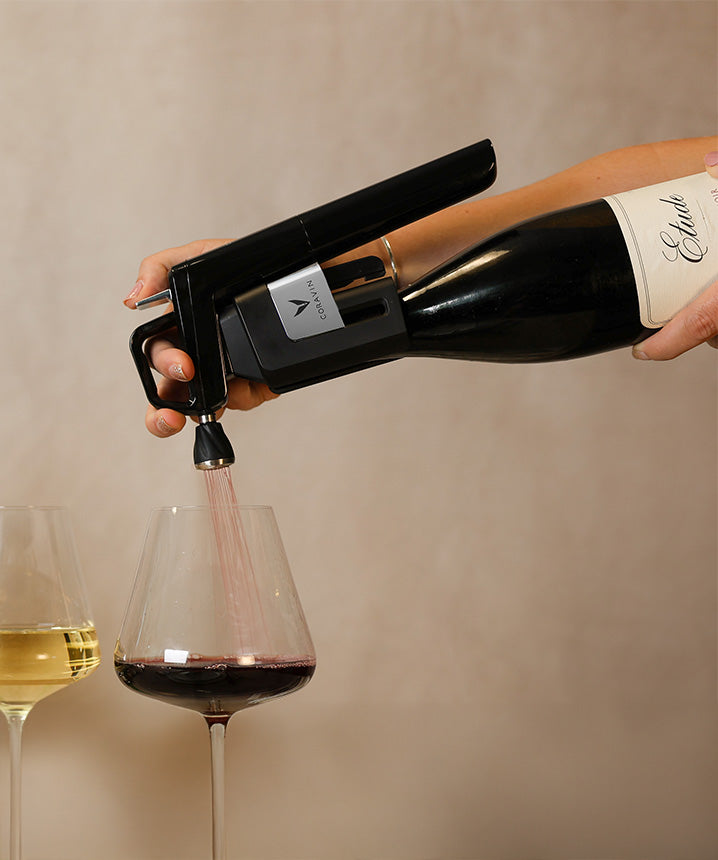 A hand holding a wine aerator pours red wine into a glass, with a white wine glass next to it.
